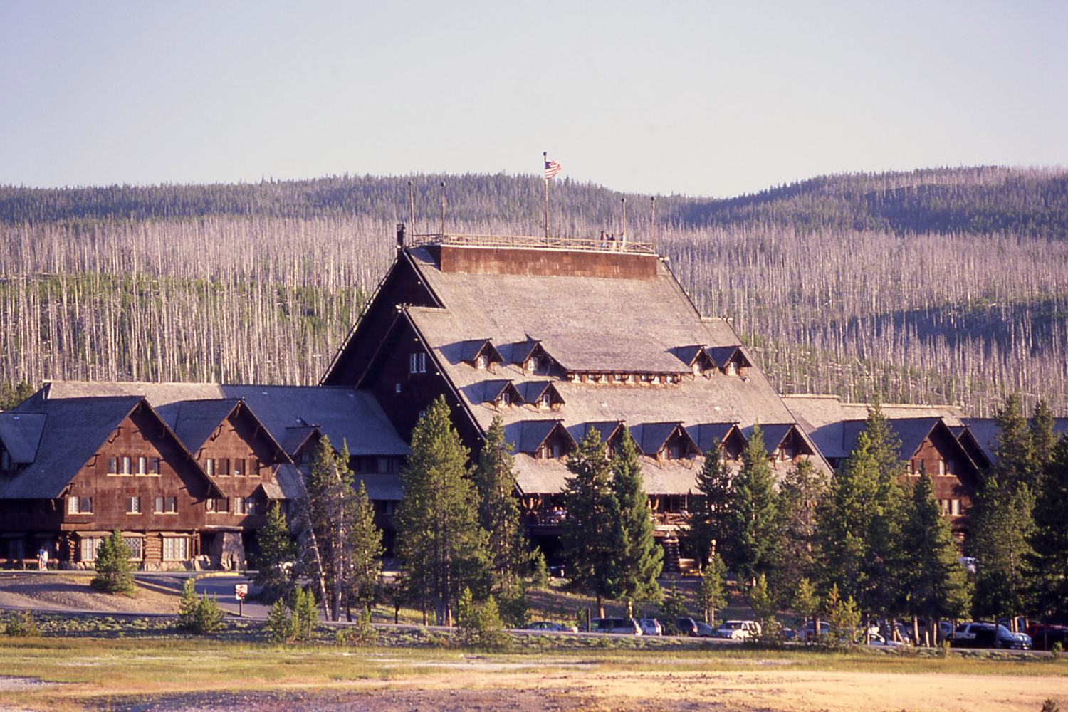 The steep log gables of the Old Faithful Inn above a meadow with burned timber on the ridge behind.